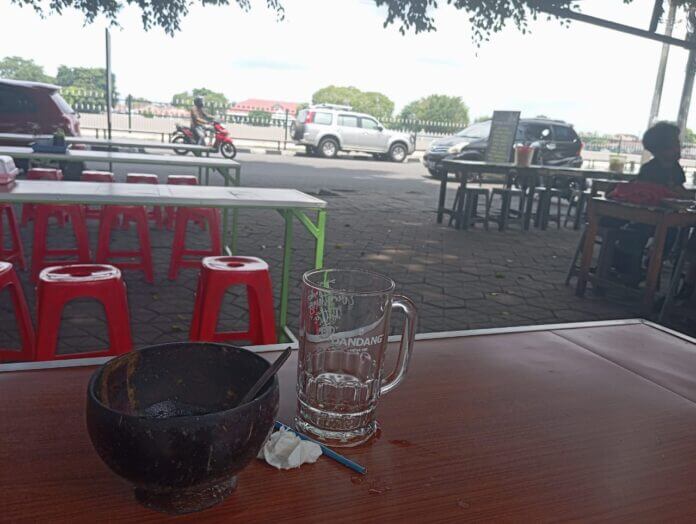 Meja makan kosong setelah wisatawan selesai makan, dengan sisa mangkuk dan gelas kosong di atas meja kayu.